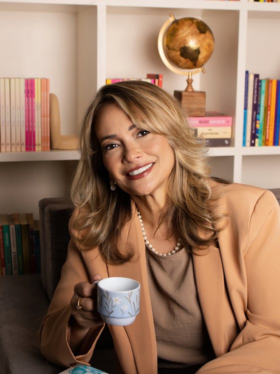 Cinthia Sàntiago sorrindo, segurando uma xícara de café no consultório.